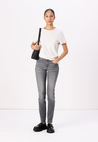 Lys grå t-shirt med et tekstureret logo, parret med tætsiddende mørkegrå jeans og kraftige sorte loafers. Enkel sort skuldertaske.