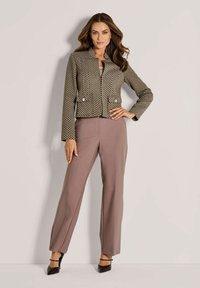 Bruine geprinte jas met een cropped ontwerp, twee voortassen en zilveren knopen, gecombineerd met tapered beige broeken en zwarte hakken.