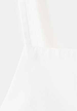 Prim-plan al unui articol vestimentar alb, cu un decolteu drept și o bretelă subțire, evidențiind textura materialului și detaliile cusăturilor.