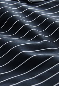 Marineblauwe stof met witte golvende strepen, met een gladde textuur en zachte plooien. Het ontwerp toont afwisselende krommingspatronen over het oppervlak.