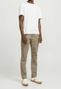 Bílé tričko s kulatým výstřihem, světle hnědé kalhoty, béžové a bílé tenisky. Jednoduchý design bez viditelných vzorů nebo log. Hladká texturovaná látka.