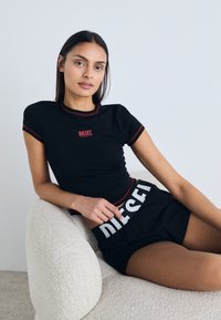 T-shirt preta ajustada com bainha vermelha e logótipo "DIESEL" no peito, combinada com calções pretos com letras brancas "DIESEL" na cintura.
