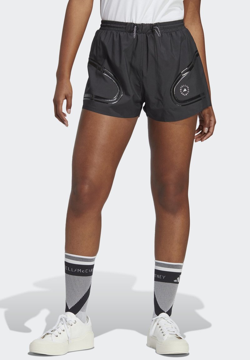 Shorts sportivi neri con vita elasticizzata, due tasche laterali e dettagli riflettenti. Abbinati a sneakers bianche e calzini con fantasia.