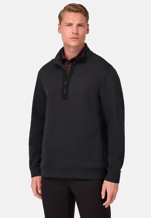 Pulóver negro de media cremallera hecho de un tejido suave, con un cuello alto, mangas largas y detalles en paneles laterales. Líneas limpias y diseño minimalista.