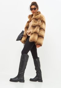 Faux fur coat with brown stripes, beige sweater, black skinny jeans, and knee-high black leather boots, accessorized with black sunglasses and clutch.