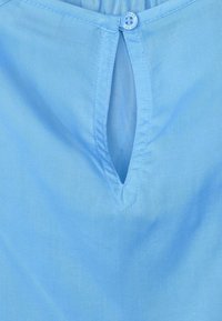 Lichtblauwe blouse met een sleutelgatopening, een knoopsluiting en een zachte textuur. De halslijn is afgerond en de stof oogt glad.