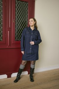 Denim shirt dress with long sleeves, two chest pockets, in dark blue. Paired with knee-high black boots and gray knee socks. Wood floor.