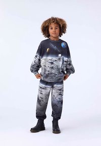 Sada mikiny a kalhot s vesmírným motivem obsahujícím grafiku planety a lunární povrchu; navrženo v šedé barvě s černými akcenty.