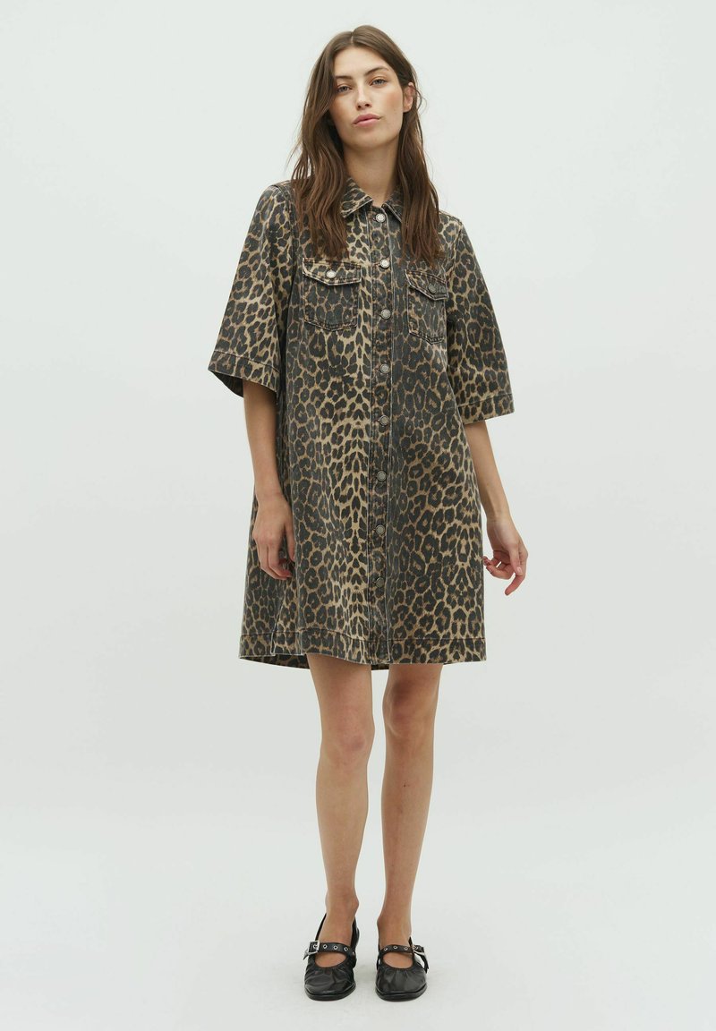Leopardprint denim jurk met korte mouwen, knopen aan de voorkant en twee borstzakken. Kleuren zijn bruin, tan en zwart in een patroon.