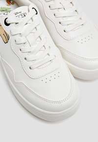 White sneakers with a smooth leather finish, featuring round laces, perforated toe box, and Disney-themed design on the tongue.