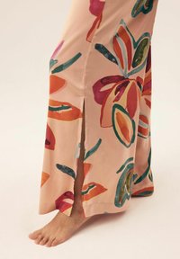 Długa sukienka kwiatowa w pastelowym różowym kolorze z dużymi, wielokolorowymi wzorami kwiatowymi, z rozcięciem po boku oraz gładką, satynową teksturą.