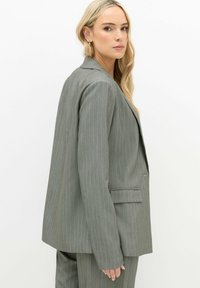 Grijze pinstripe blazer met een gestructureerde pasvorm, notch revers en twee voorkzakken. Smooth textuur met subtiele blauwe accenten in de strepen.