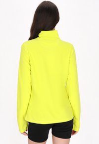 Langærmet pullover med høj krave i klart neon-gul stof med en glat tekstur. Har et tætsiddende design og diskrete sømdetaljer.