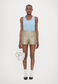 Plavi pleteni top bez rukava, zlatne šortse s bijelim cvjetnim uzorkom i svijetlopinkasta torba s naglascima u obliku mašne. Bijele čarape i crne cipele upotpunjuju izgled.