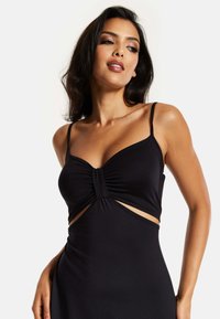Black dress with adjustable spaghetti straps, ruched bodice detail at the center, cut-out sides, and a smooth, fitted silhouette.