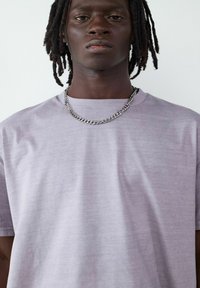 Szara koszulka z krótkim rękawem wykonana z miękkiego materiału, z okrągłym dekoltem i gładką teksturą, w zestawie z srebrnym naszyjnikiem.