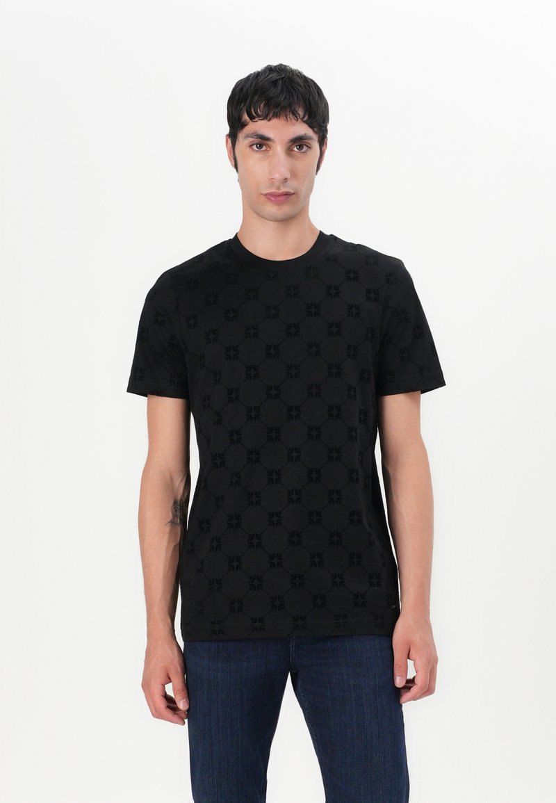 T-shirt en coton noir avec un motif texturé ton sur ton. Manches courtes et encolure ronde. Porté avec un jean en denim foncé.