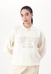 Sudadera color crema con cuello, con el texto bordado "Converse Chuck Taylor All Star". Tejido ligero, corte relajado.