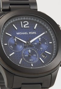 Montre Michael Kors avec un bracelet en acier inoxydable noir. Le cadran rond bleu marine texturé présente des index horaires blancs, des sous-cadrans de chronographe et une fenêtre de date.