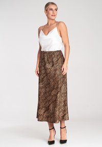 Biała satynowa koszulka na ramiączkach z cienkimi paskami, zestawiona z długą spódnicą w wzór lamparta. Spódnica ma gładką teksturę i dopasowany pas.