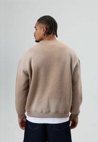 Beige oversized sweatshirt met geribbelde boorden aan de mouwen en zoom, gemaakt van een katoenmix, voorzien van een ronde hals en doorlopende schoudernaden, gedragen over een wit shirt.