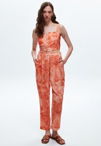 Twee-delige outfit met een cropped, knoopsluitend, mouwloos topje en hoge, wijde broek met een lichtoranje bloemenpatroon.