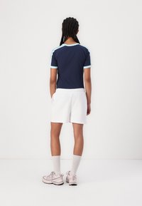 Top atletico blu navy con dettagli azzurri, abbinato a pantaloni corti bianchi. Modella che indossa sneakers rosa e calzini grigi al ginocchio.