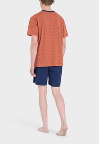 T-shirt arancione a maniche corte con un piccolo design a pattern, abbinato a pantaloni corti blu scuro. Presenta un colletto blu navy e una vestibilità comoda.
