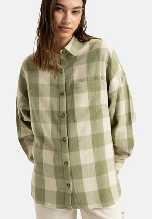 Hnědozelená kostkovaná flanelová košile s límečkem, předními knoflíky a náprsní kapsou s logem, vyrobená z měkkého materiálu.