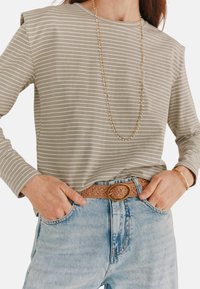 Gråstribet langærmet skjorte med afslappet pasform, parret med lyseblå jeans og et vævet brunt bælte med en rund guldspænde.