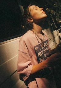 Różowy, przejrzysty t-shirt z grafiką i tekstem, noszony z warstwą naszyjników; naturalne światło podkreśla strukturę materiału.