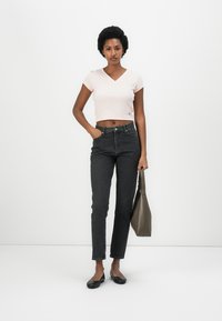 Top corto rosa a scollatura a V abbinato a jeans in denim neri a vita alta e scarpe nere flat, mentre tiene una borsa grigia. Design semplice e aderente.