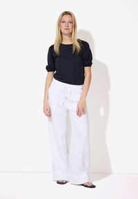 Marineblauwe top met pofmouwen gecombineerd met witte linnen broek met trekkoord. De outfit heeft een losse pasvorm en een gladde textuur. Blauwe slippers voegen kleur toe.