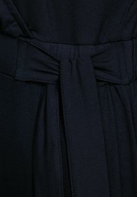 Granatowa sukienka z teksturowanej tkaniny, z detalem w postaci wiązania w talii oraz gładką sylwetką bez widocznych zapięć czy wzorów.