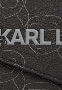 Cuir texturé noir avec une finition brillante, présentant un motif floral en relief et un logo "KARL LAGERFELD" en gris.