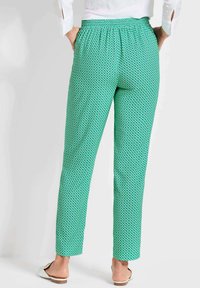 Grüne gemusterte Hose mit elastischem Bund und schmaler Passform. Der Stoff weist ein geometrisches Design in hellgrün und weißen Akzenten auf.