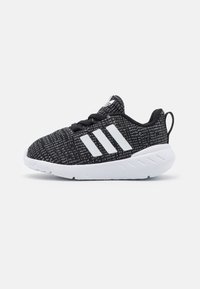 Scarpe sportive in bianco e nero con tomaia in maglia texturizzata, tre strisce bianche e suola in gomma, dotate di un linguetta sul tallone.