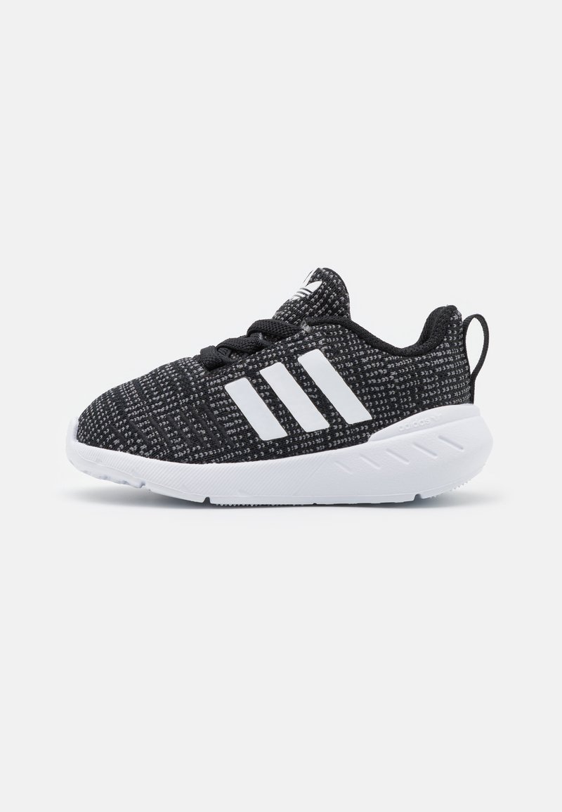 Scarpe sportive in bianco e nero con tomaia in maglia texturizzata, tre strisce bianche e suola in gomma, dotate di un linguetta sul tallone.