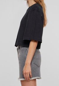 Černý krátký rukávový boxy top v kombinaci s šedými džíny šortkami s třepeným lemem a detailem zadní kapsy. Hladká textura, volný střih.