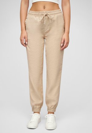 Beige jogger pants made of soft fabric, featuring an elastic waistband with drawstring, and elastic cuffs at the ankles. Worn with white sneakers.
