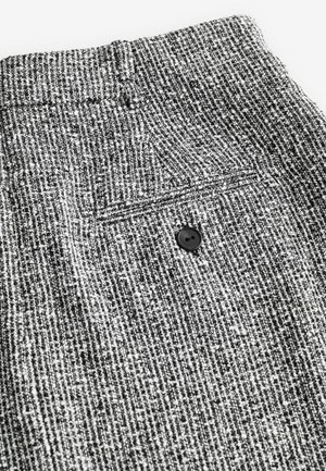 Texturovaná černobílá látka se jemným kostkovaným vzorem, obsahující černý knoflík a zadní kapsu na pase.