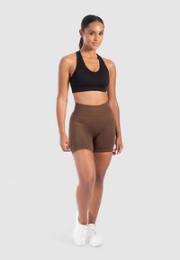 Sort sports-bh med rund halsudskæring kombineret med brune, højtaljede shorts med sidelomme. Modellen står på en lys baggrund.