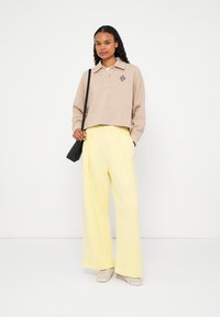 Sweatshirt polo cropped bege com um design bordado, combinado com calças amarelas de perna larga de cintura alta e sapatos bege claro.