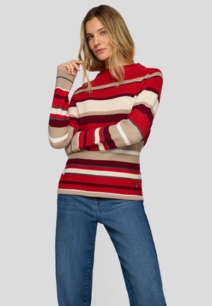 Roter und beiger gestreifter Pullover mit hohem Kragen, geripptem Strickmuster und langen Ärmeln, kombiniert mit blauen Jeans.