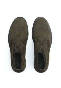 Chaussures en daim vert olive avec un bout arrondi, deux œillets et des lacets marron. La semelle est noire avec une finition texturée.