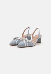 Lys blå mokkasinsko med slingback og spiss tå, sølvremmer og en sløyfe. Blokkhælen gir stabilitet og støtte.