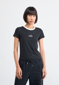 Fekete pamut póló rövid ujjakkal, fehér bordás gallérral és hímzett "nike" logóval a mellkasán. Sötét melegítőnadrággal párosítva.