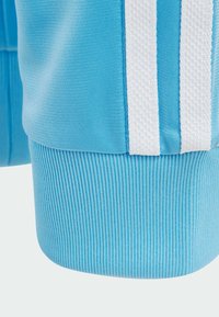 Pantalones deportivos de color azul claro con rayas blancas, que cuentan con una tela texturizada y puños de tobillo acanalados para un ajuste seguro y comodidad.