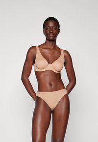 Nude-colored bra and matching panties set made of smooth fabric, featuring a simple design with wide straps and a delicate lace pattern.