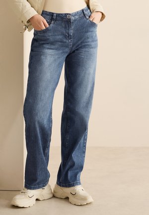 Pantalon en denim bleu clair avec des rayures verticales, design à jambe droite, cinq poches et fermeture à bouton. Porté avec des baskets blanches.
